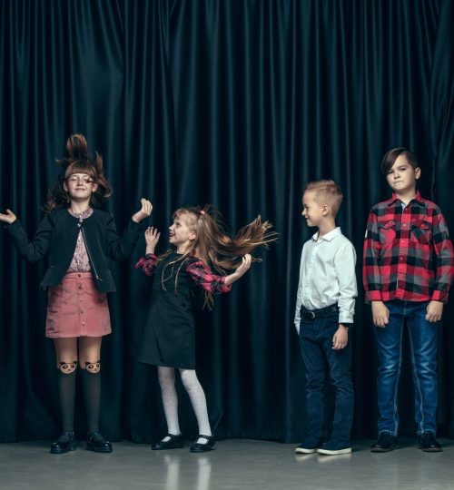 Cute surprised stylish children on dark background. Beautiful stylish teen girls and boy standing together and posing on the school stage in front of the curtain. Classic style. Kids fashion and emotions concept.